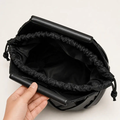 Vista interna da bolsa feminina Iris em couro trançado preto da Nualle, segurada aberta para mostrar o forro macio de tecido escuro com fechamento prático e seguro em cordão.