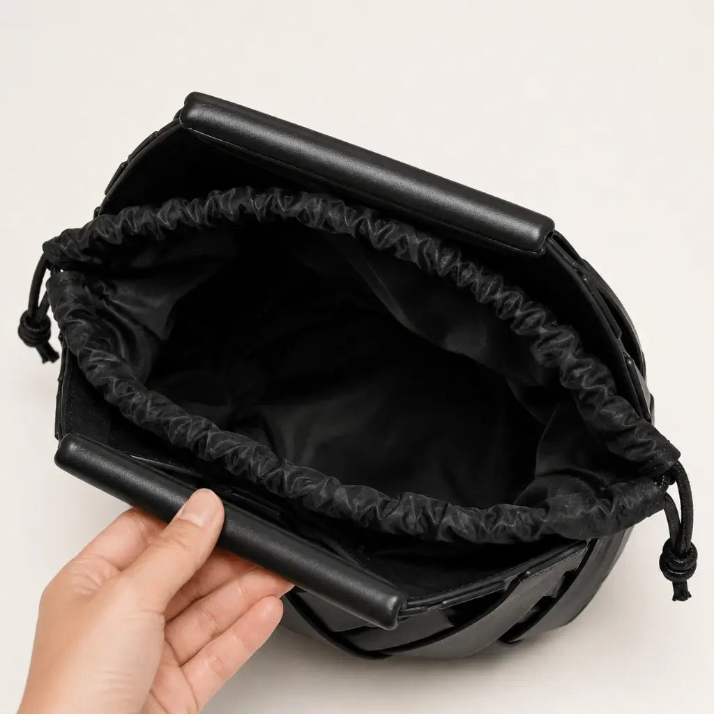 Vista interna da bolsa feminina Iris em couro trançado preto da Nualle, segurada aberta para mostrar o forro macio de tecido escuro com fechamento prático e seguro em cordão.