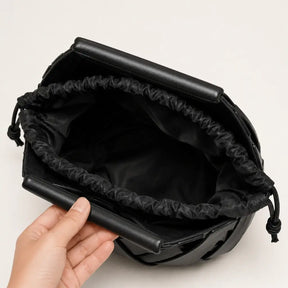 Vista interna da bolsa feminina Iris em couro trançado preto da Nualle, segurada aberta para mostrar o forro macio de tecido escuro com fechamento prático e seguro em cordão.