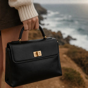 Close-up da Bolsa Feminina em Couro Preta Louise em mão feminina destacando o fecho giratório dourado e o couro liso premium