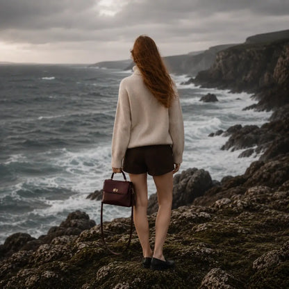 Modelo caminhando entre pedras usando a Bolsa Feminina em Couro Louise Bordô no estilo crossbody de luxo.