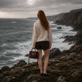 Modelo caminhando entre pedras usando a Bolsa Feminina em Couro Louise Bordô no estilo crossbody de luxo.