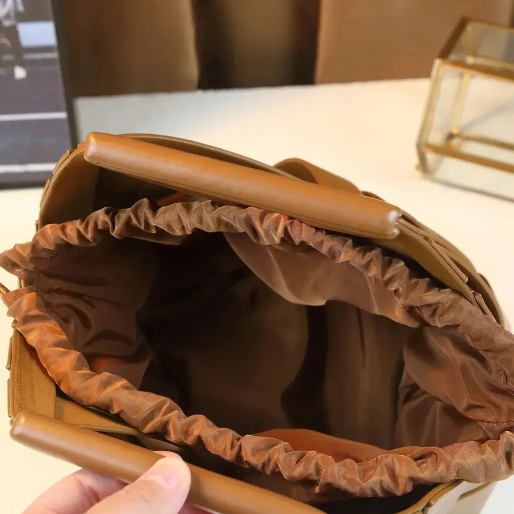 Bolsa feminina marrom caramelo de couro trançado, mostrada com o interior forrado em tecido de tom terra e o fechamento por cordão ajustável aberta