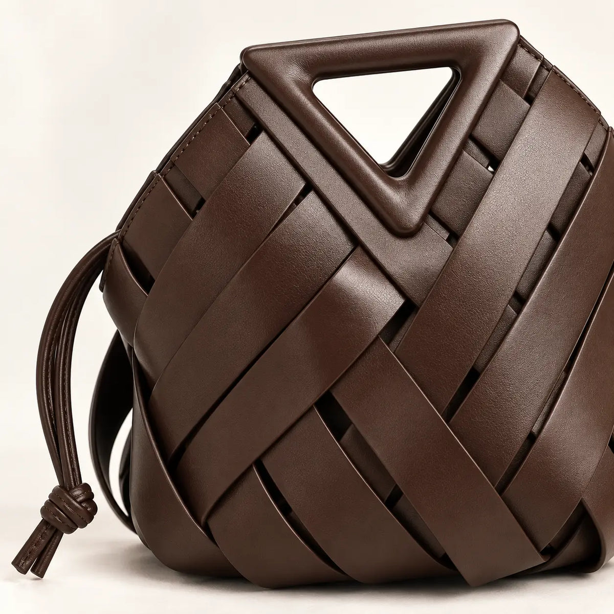 Detalhe da trama em couro coffee e da alça triangular estruturada da Bolsa Iris