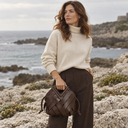 Mulher elegante com a Bolsa Iris Coffee em cenário editorial na costa rochosa