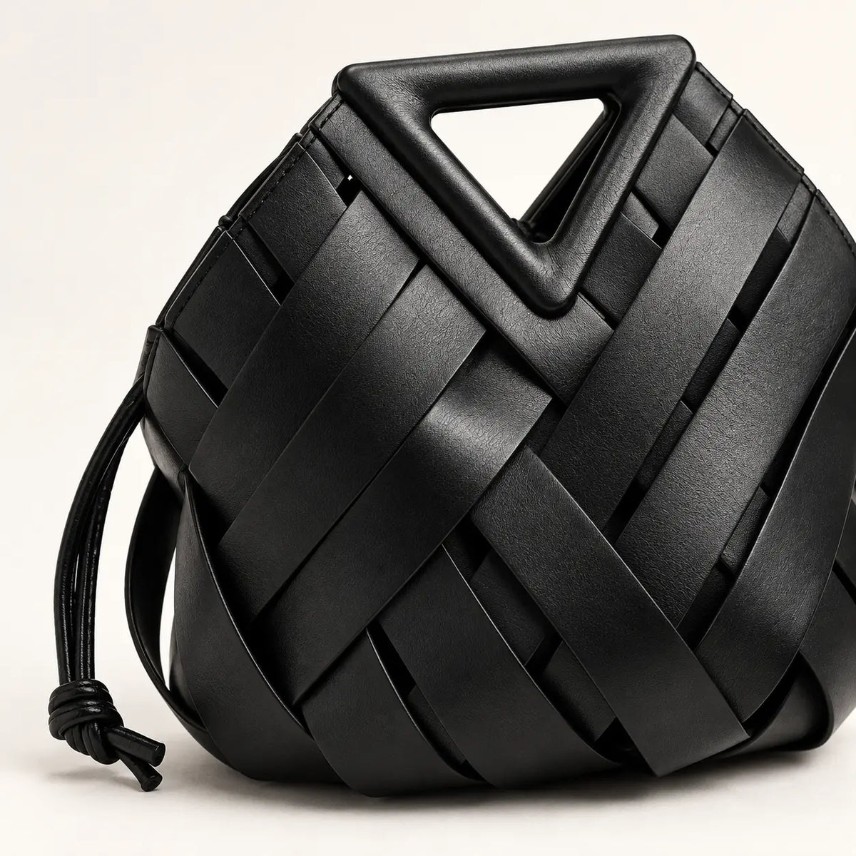Detalhe da trama em couro preto e da alça triangular estruturada da Bolsa Iris