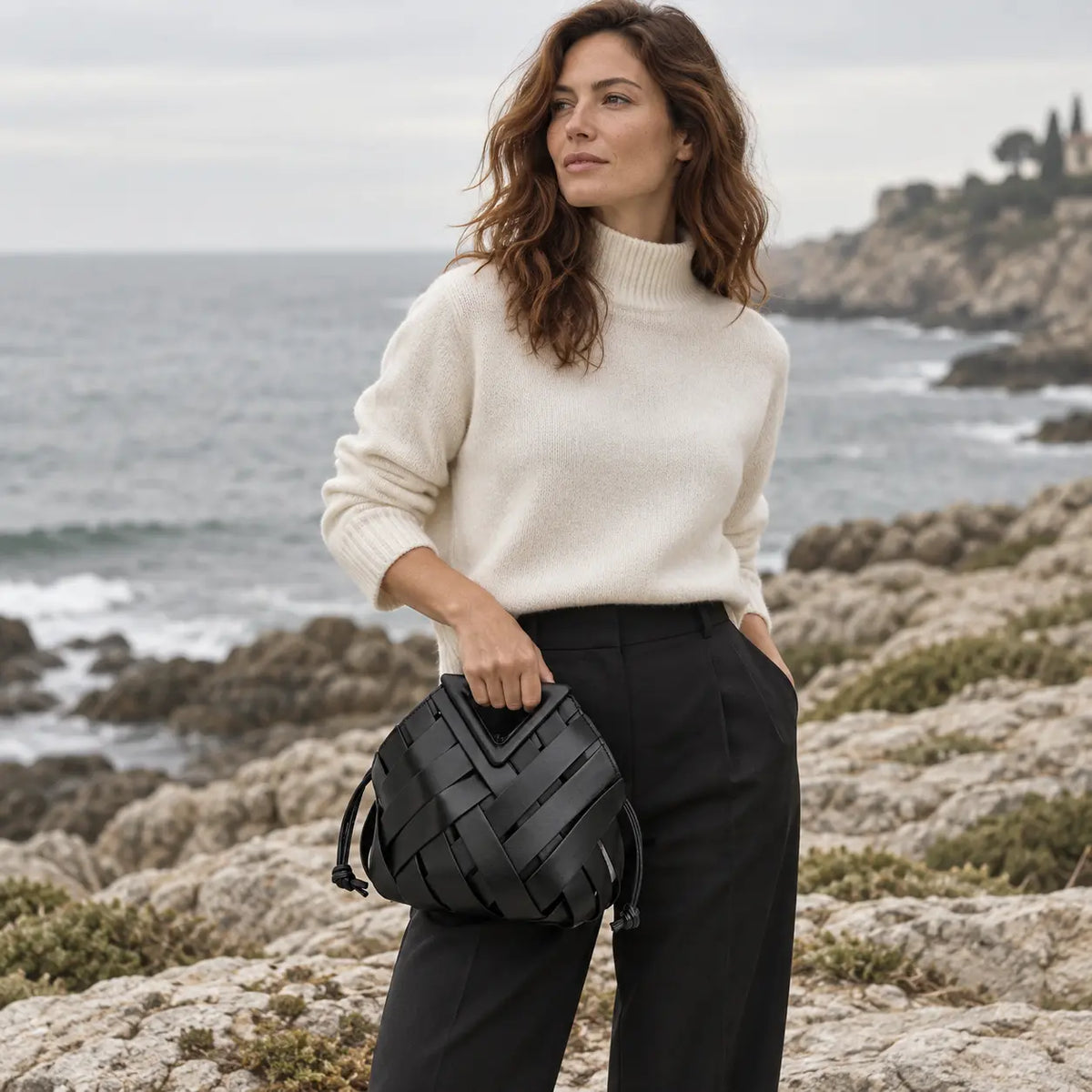 Mulher elegante com a Bolsa Iris Preta em cenário editorial na costa rochosa