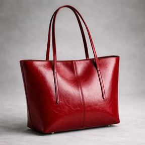 Bolsa tote feminina  em couro texturizado na cor vermelho tomate, vista lateralmente em um fundo cinza.