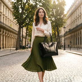 Mulher elegante com saia plissada verde oliva e bolsa tote de couro preto caminhando em boulevard parisiense com luz dourada