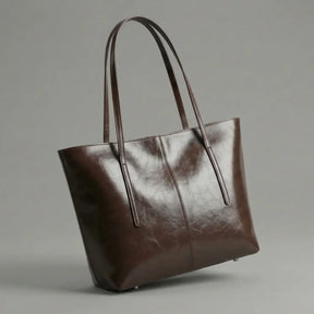 bolsa Tote Élise em couro marrom café no ombro. A imagem destaca o tamanho generoso da bolsa e como ela se ajusta confortavelmente ao corpo, ideal para um look de trabalho sofisticado."