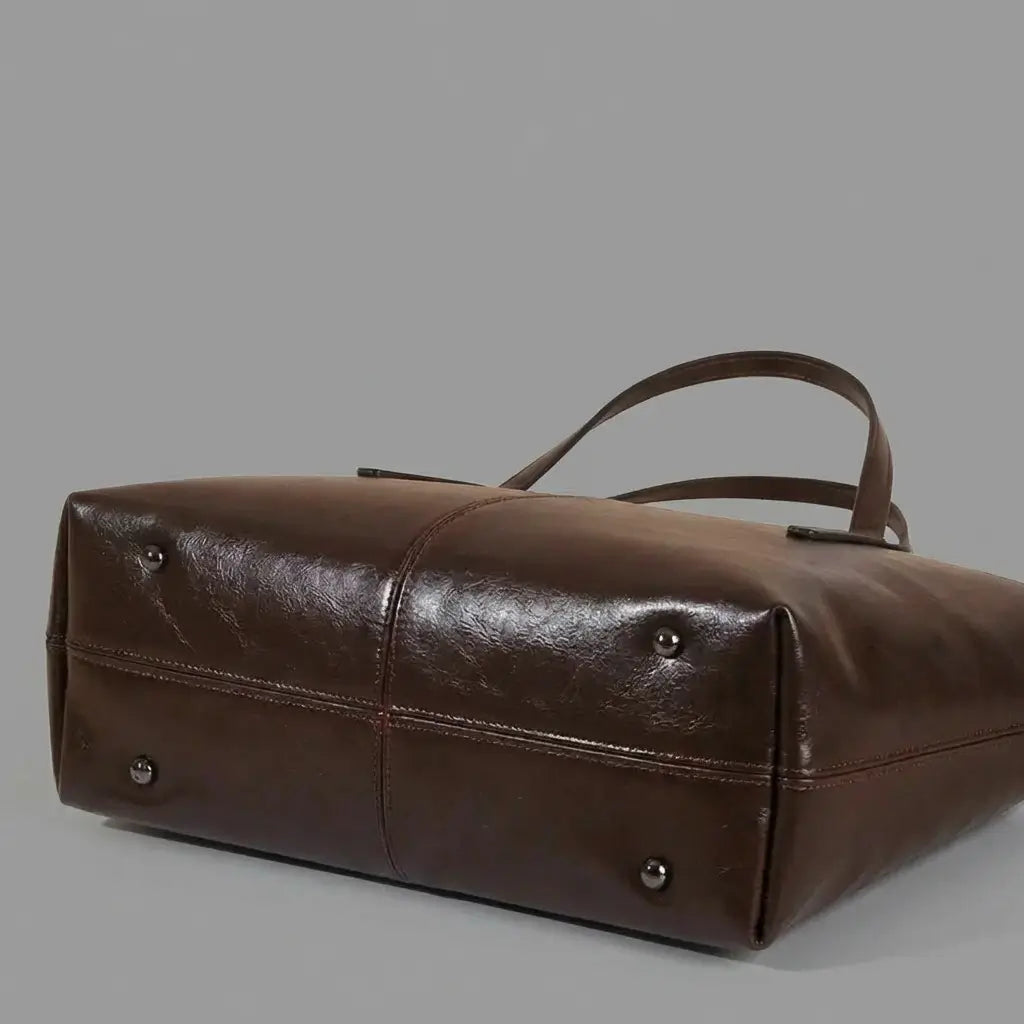 Detalhe inferior da bolsa Élise marrom mostrando os cravinhos de metal e acabamento da base.