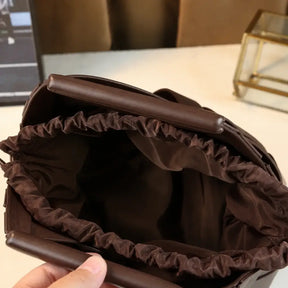 Interior da bolsa de couro marrom escuro aberta mostrando forro franzido em tecido e alça rígida triangular, vista de cima